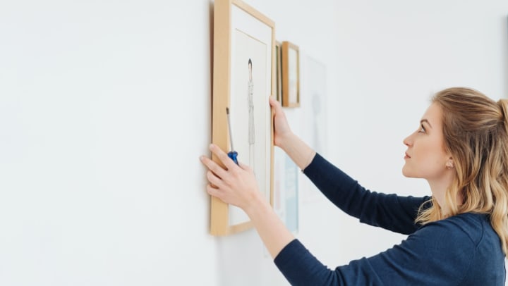 Concentrating woman hanging a wooden-framed picture on a white wall.