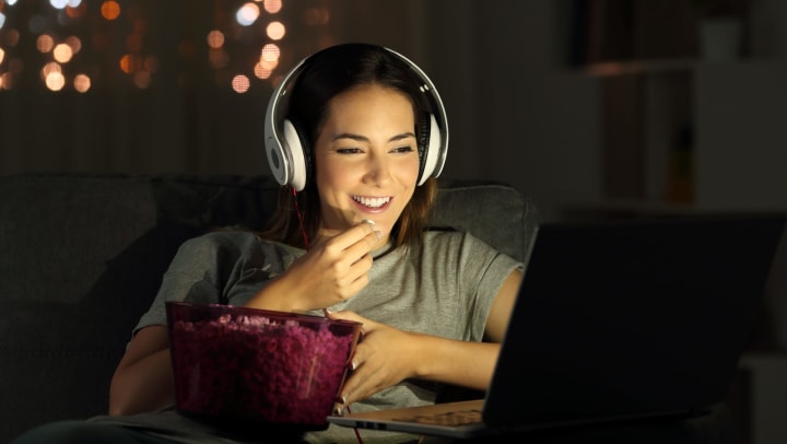 Person eating popcorn, watching movies on laptop.