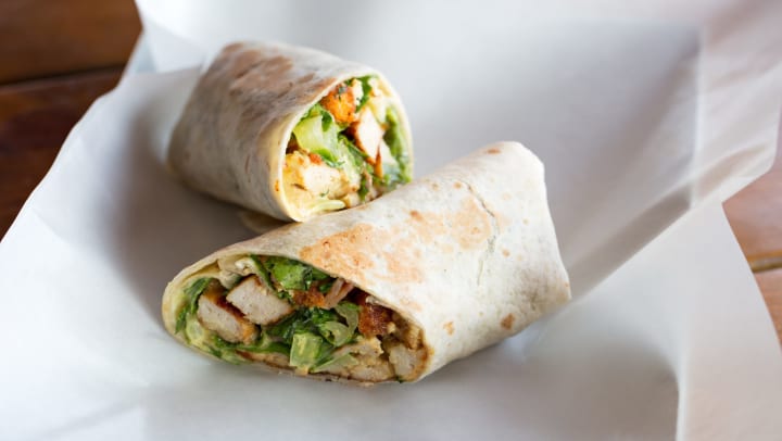 Chicken Caesar salad sandwich wrap on a white parchment paper.