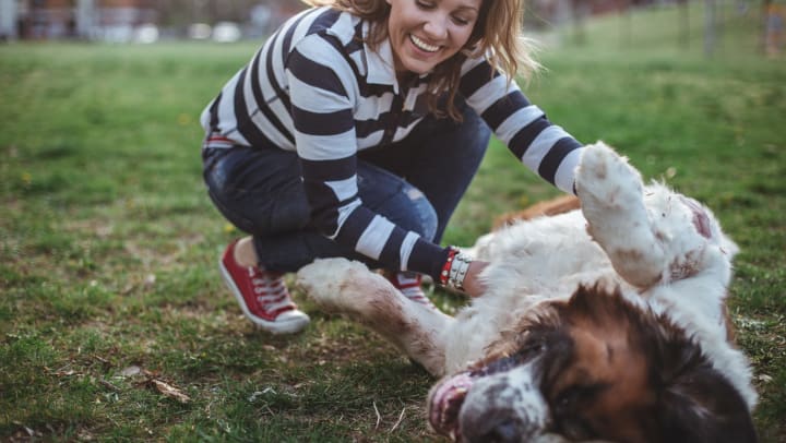 Woman petting a dog’s belly and smiling while outdoors.