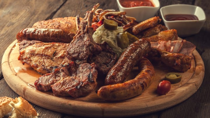 An assortment of grilled meats on a wooden platter with a bread roll and two dishes of red dipping sauces