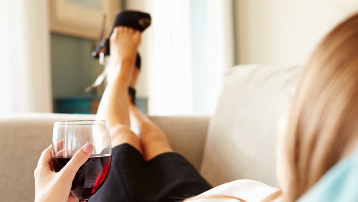 Woman lounging on a couch kicking her feet up, with a glass of red wine.