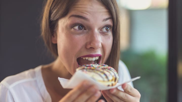 Woman holding a donut on a napkin with mouth open, seemingly about to take a bite. 