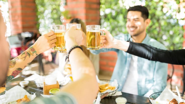 Group of young friends with drinks celebrating at an outdoor restaurant.