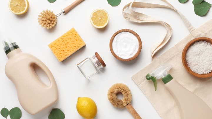 Overhead view of household cleaning supply ingredients, a sponge, lemon, and salt on a white background