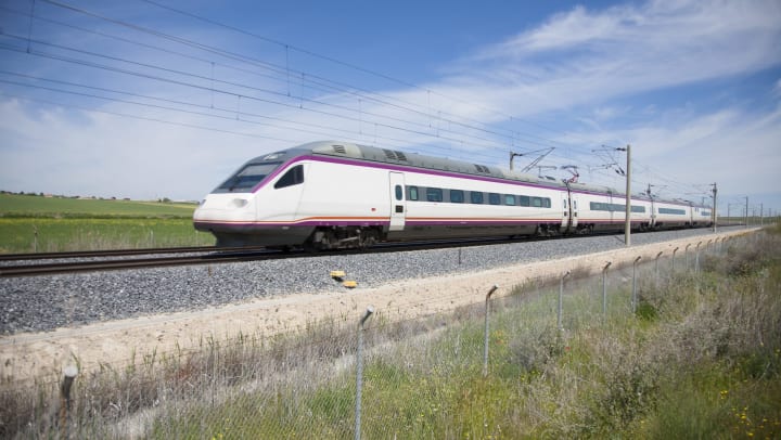 A white bullet train moving fast with green fields in the background. 