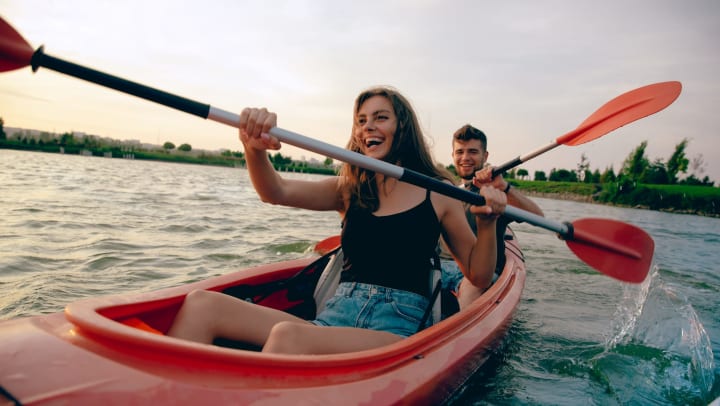 A smiling young woman and man are kayaking on the river together at sunset.