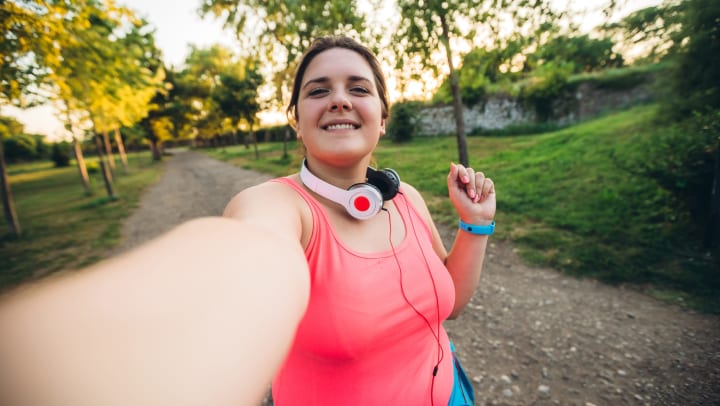 Woman on a run with headphones around her neck, smiling and taking a selfie 