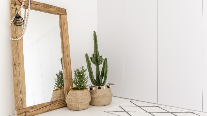White room with geometric rug, wooden framed mirror, and decorative cacti in woven baskets.