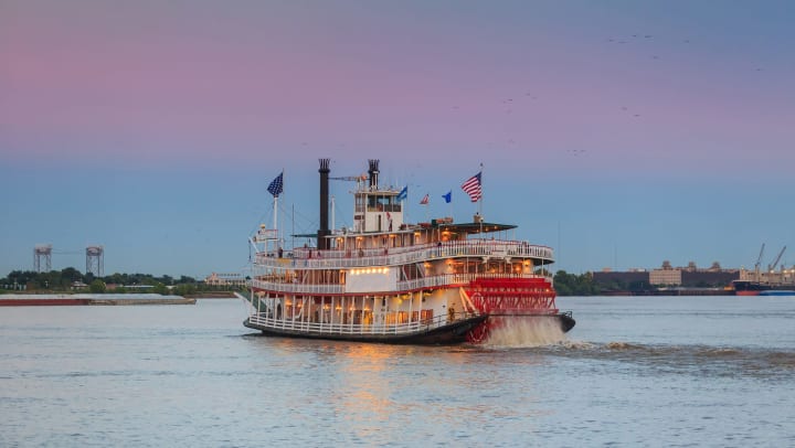 A paddle steamer floating along the water at dusk.
