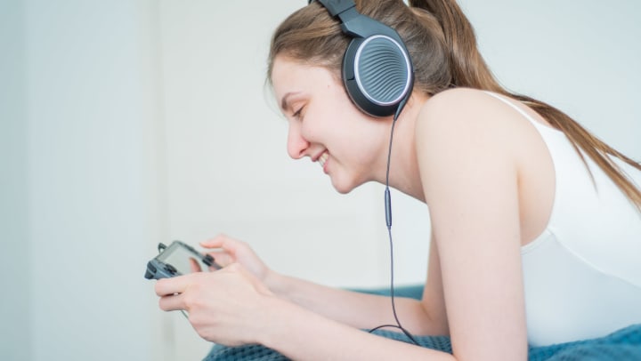 Woman playing handheld Nintendo Switch, wearing headphones