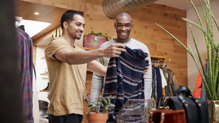 Two men in a store,  looking at a sweater and smiling.