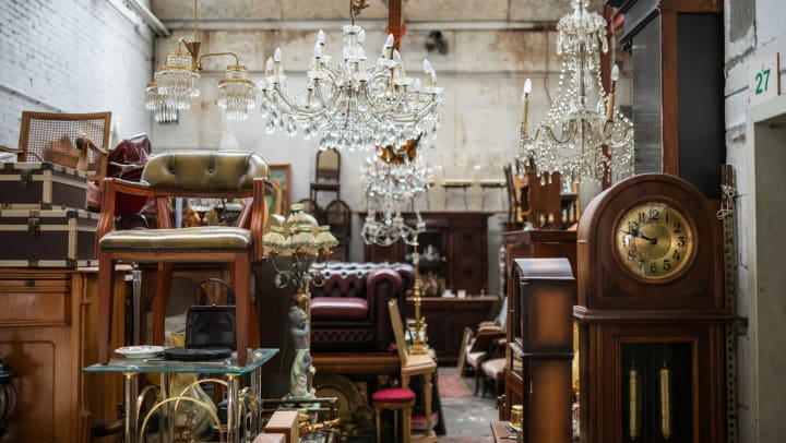 An assortment of vintage furniture and chandeliers stacked in a warehouse space. 