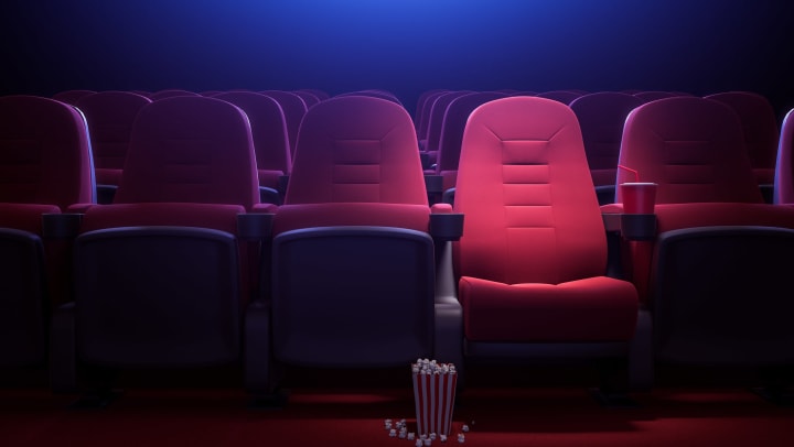 Row of empty red cinema seats, bucket of popcorn on floor by open seat