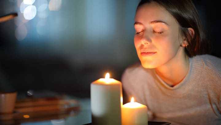 A woman with her eyes closed smells two scented candles on a table.