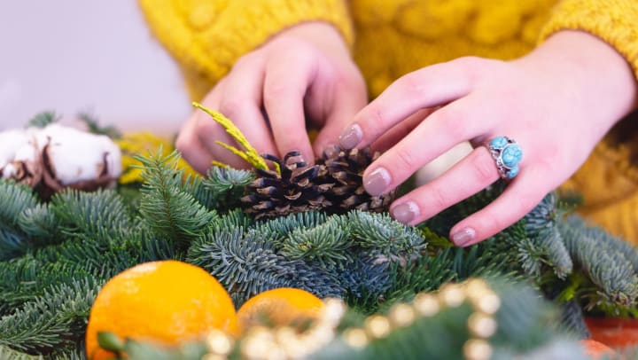 Close up of a woman decorating faux greenery with lemons, gold beads, and pine cones.