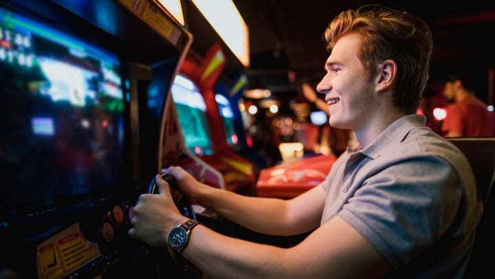 Man with hands on an arcade steering wheel, smiling at the lit up screen.