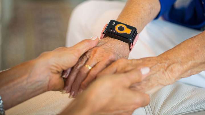 picture of two pairs of hands holding each other with one person wearing a CarePredict Tempo
