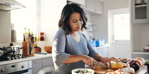 Woman chopping fresh vegetables in her vibrant, electric kitchen at Kernwood Terrace in Los Angeles, California