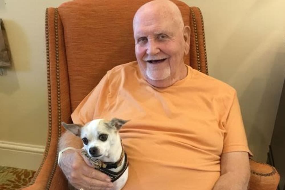 Resident male smiling in orange shirt holding dog in pet friendly assisted living community | Pathway to Living