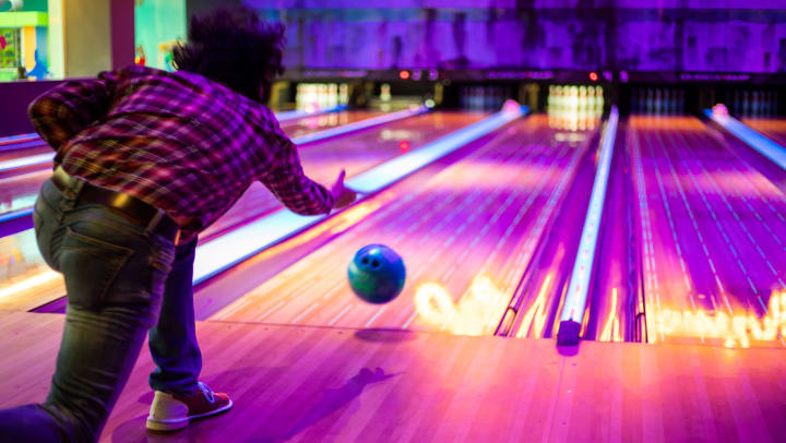A lone bowler releases a bowling ball down a neon-colored lane during a game of black light bowling