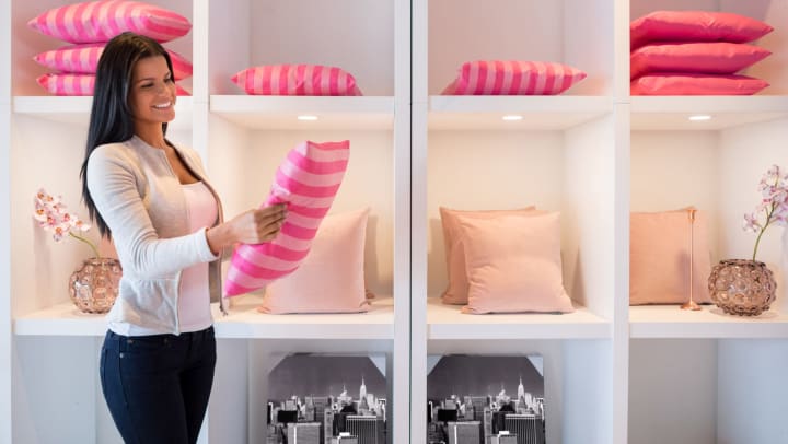 A young woman shopping at a home decor store considers a pink, striped pillow.