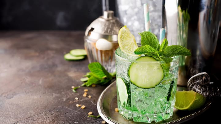 Mojito cocktail with lime and mint in highball glass on a dark stone background served with brown sugar and shaker
