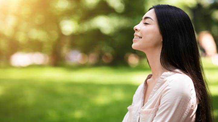 Profile view of smiling young woman with eyes closed in a green sunlit park