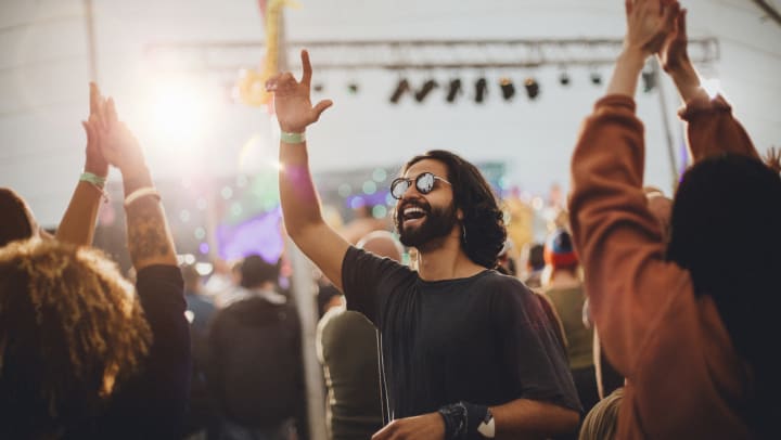 A man in a crowd waving at someone. A band stage is in the background.