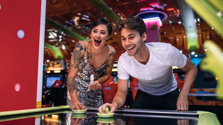 Young man and young woman playing air hockey in a colorful indoor arcade