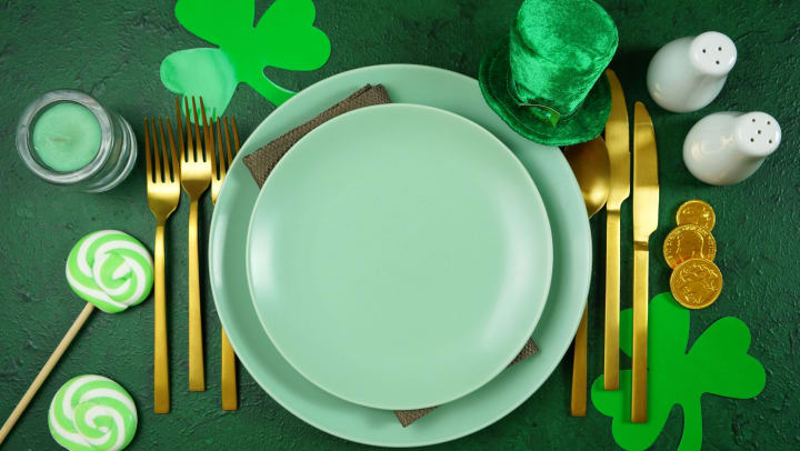 A St. Patrick’s Day-themed dinner plate with utensils, salt and pepper shaker, candle, lollipops, coins, a small green hat, and a paper shamrock. 