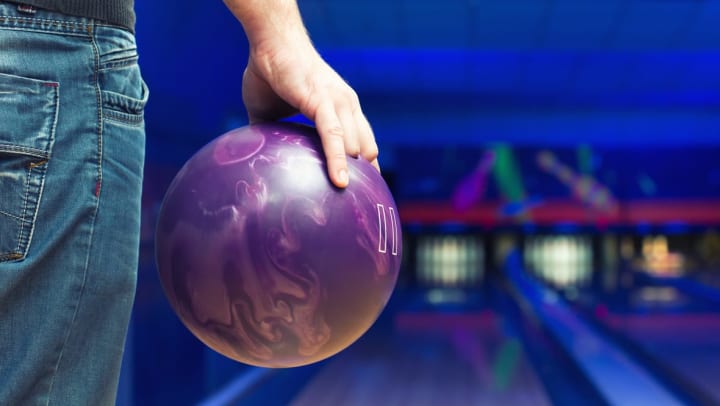 A close up of a man’s hand holding a bowling ball while standing at a bowling alley lane.