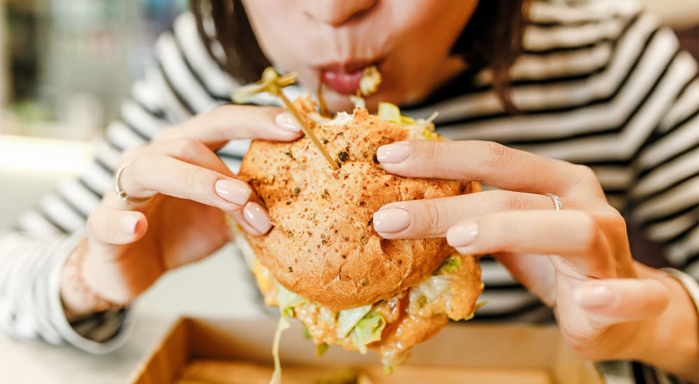 A woman eating a cheeseburger near Retreat at the Park in Burlington, North Carolina