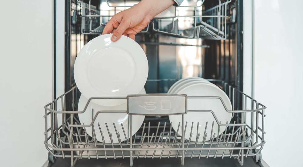 Person placing a white plate into the lower rack of a modern dishwasher at Woodlawn Lofts in Pittsburgh, Pennsylvania