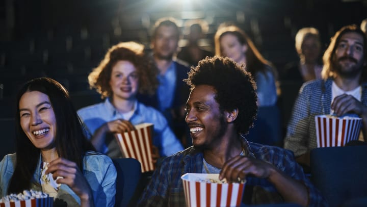  People laughing and eating popcorn while watching a film in a movie theater