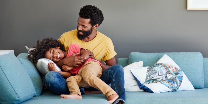 A father and his daughter playing on a couch in a home at Covenant Trace in Newport News, Virginia