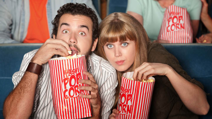 A man and a woman eating popcorn in a movie theater