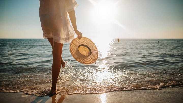 Woman holding a sun hat at the beach by the water