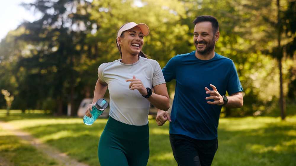 Two joggers smiling on a green path surrounded by trees, enjoying an active lifestyle at Lakewood Villas in Bossier City, Louisiana