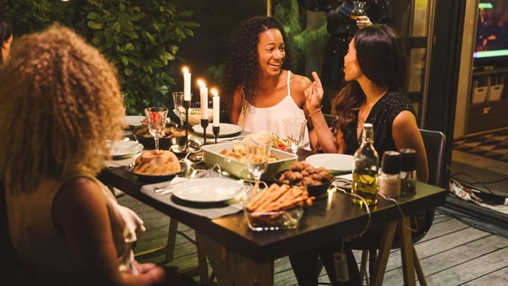 A group of smiling women have a dinner party in the evening.