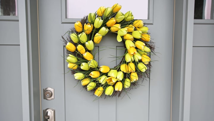 A wreath of bright yellow tulips hangs on a grey front door.