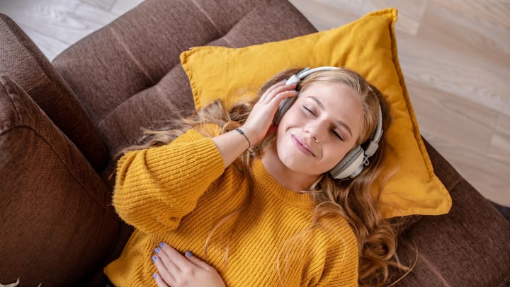 A woman laying on a couch with headphones on, listening to music.