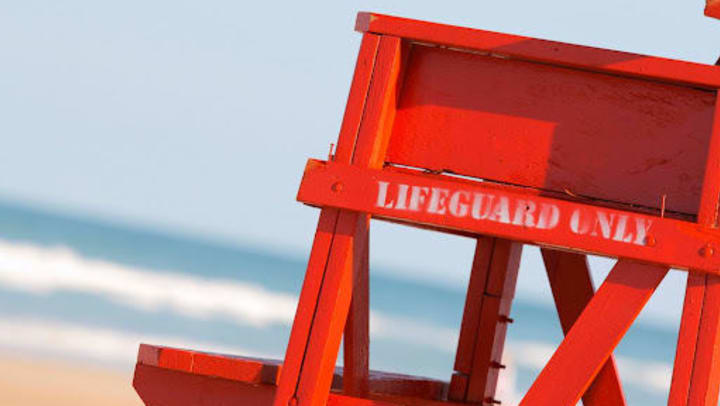 Close-up view of a red lifeguard chair on a sunny beach with blue waves in the background