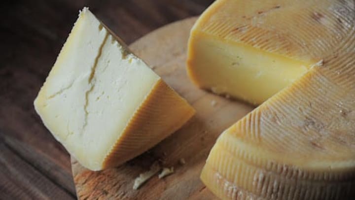A freshly cut wedge sits beside a block of artisan cheese on a circular wood cutting board