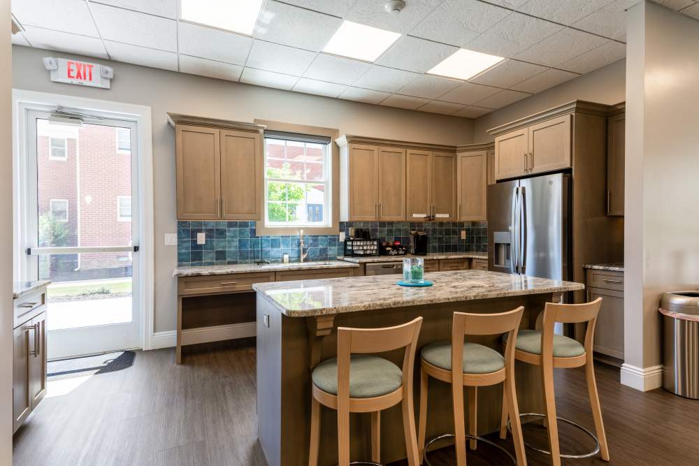Community kitchen with wood cabinetry, granite island with bar seating, stainless steel appliances, and tiled backsplash at Center Grove Village in Randolph, New Jersey.