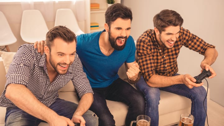 Three men on the couch cheering. Two of the men have game controllers in their hands.
