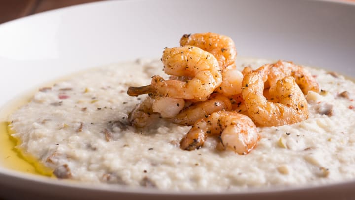 A close up shot of shrimp and grits in a white ceramic bowl on a wooden table.