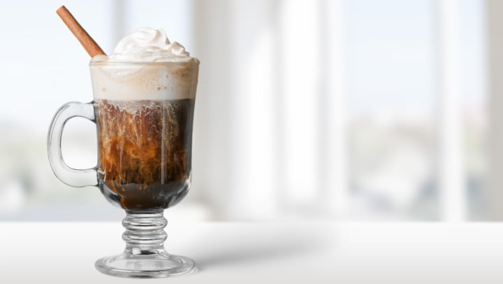 Coffee in a glass mug with whip cream and a cinnamon stick