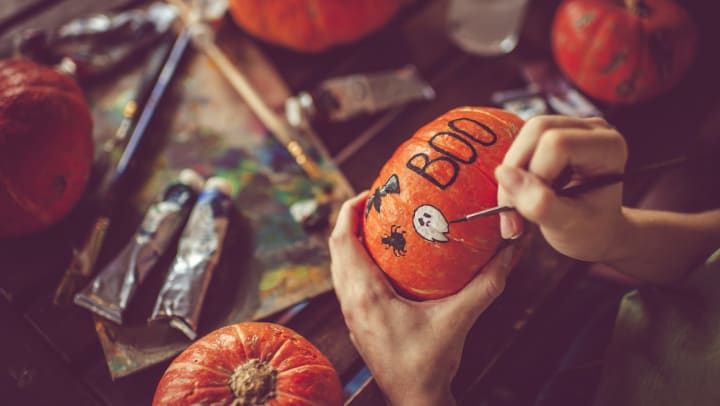 Person painting pumpkin, with paint supplies and other pumpkins sitting on table.