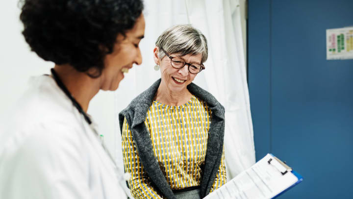 Smiling doctor holding a clipboard and talking to older smiling woman in a doctor’s office